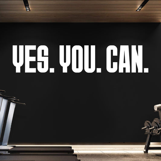 Motivational quote 'YES. YOU. CAN.' on a black wall in a gym setting.