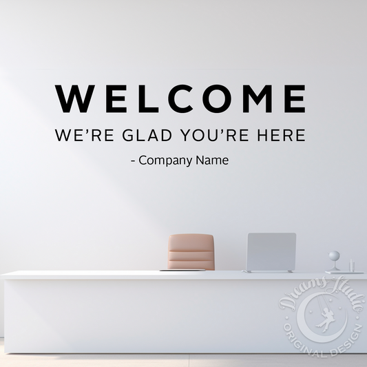 Welcome sign on a white wall above a reception desk with a plant and decor items.